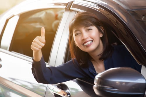 車の運転中に親指を立てる女性。 車の運転中に親指を立てる女性。