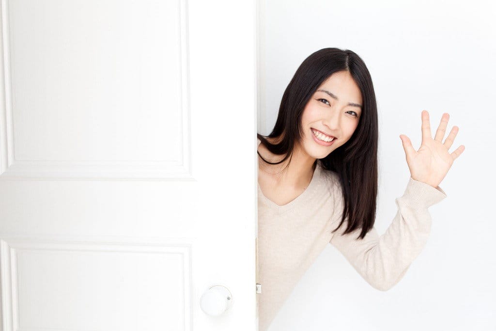 アジア系の若い女性が、ドアを少し開けて、好奇心旺盛に外を覗いている。