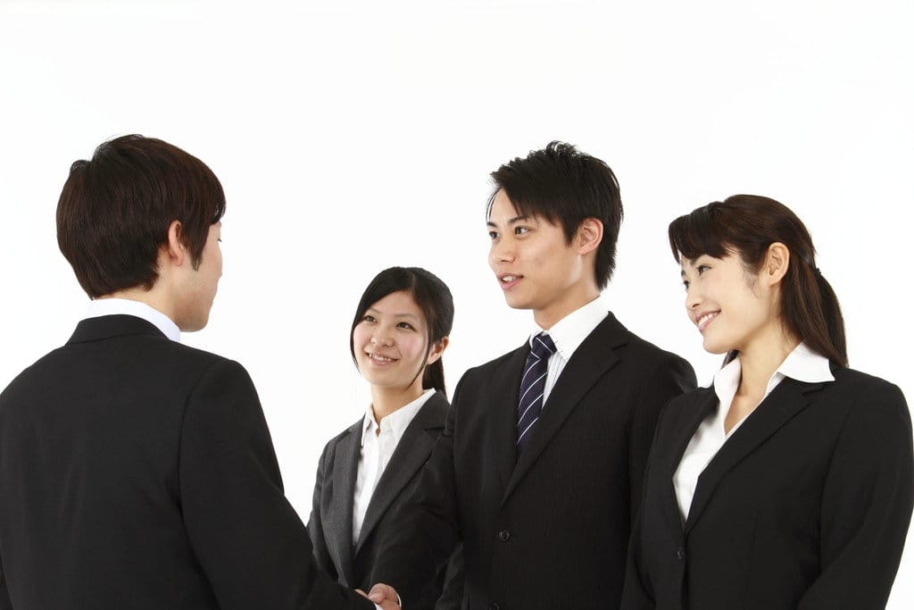 白い背景の前で握手する中国からのビジネスマンのグループ。