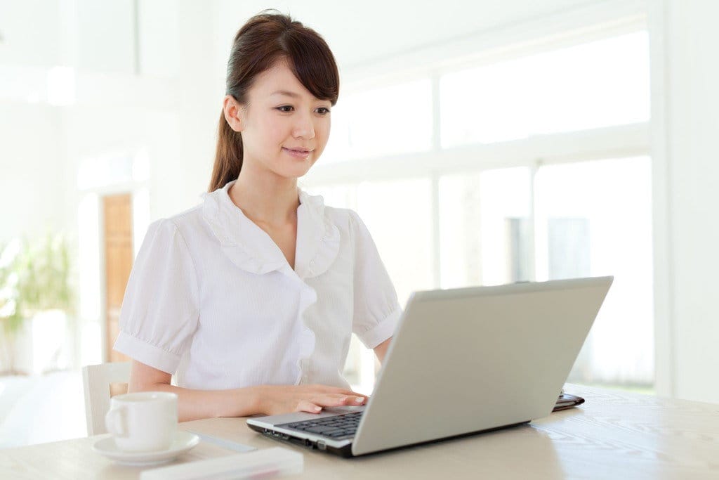 おそらく中国出身の女性が、テーブルに座ってラップトップを使用しています。