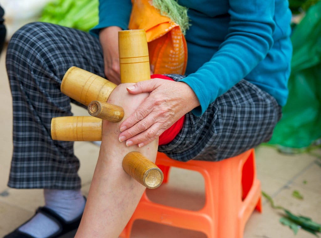 膝に竹の棒を置き、椅子に座る中国人女性。