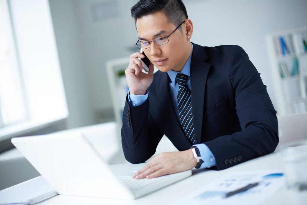 中国のスーツを着た男性が机に座りながら電話で話している。