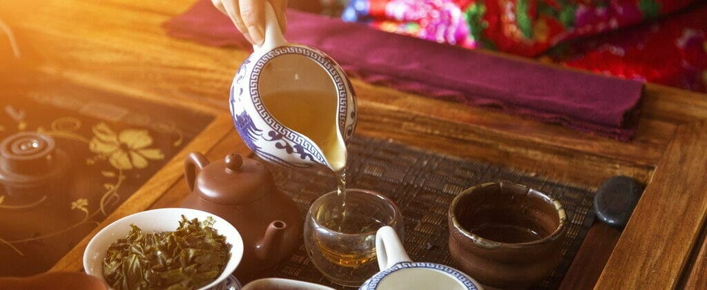 テーブルの上のカップにお茶を注ぐ中国の女性。