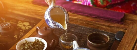 テーブルの上のカップにお茶を注ぐ中国の女性。