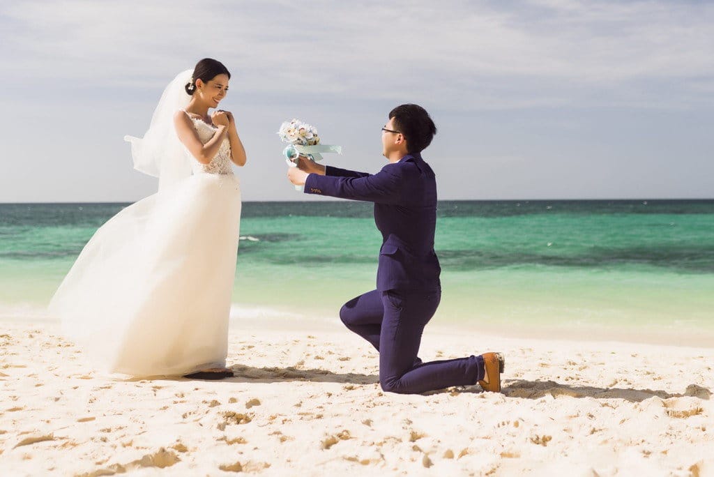 ビーチにひざまずいて女性にプロポーズする男性は、美しい景色の中でロマンチックなひとときを演出します。