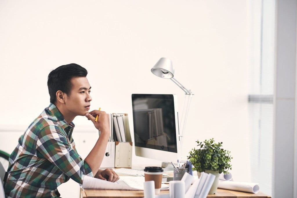 机に座って、仕事中にコンピューターの画面に夢中になっている男性。