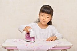 中国の小さな女の子が布地にアイロンをかけています。