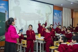 ピンクのシャツを着た女性が中国の教室で子供たちに教えている。