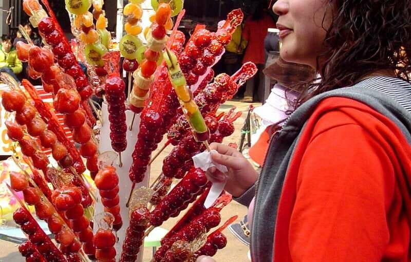 中国で果物の串がいっぱいの木を眺める女性。