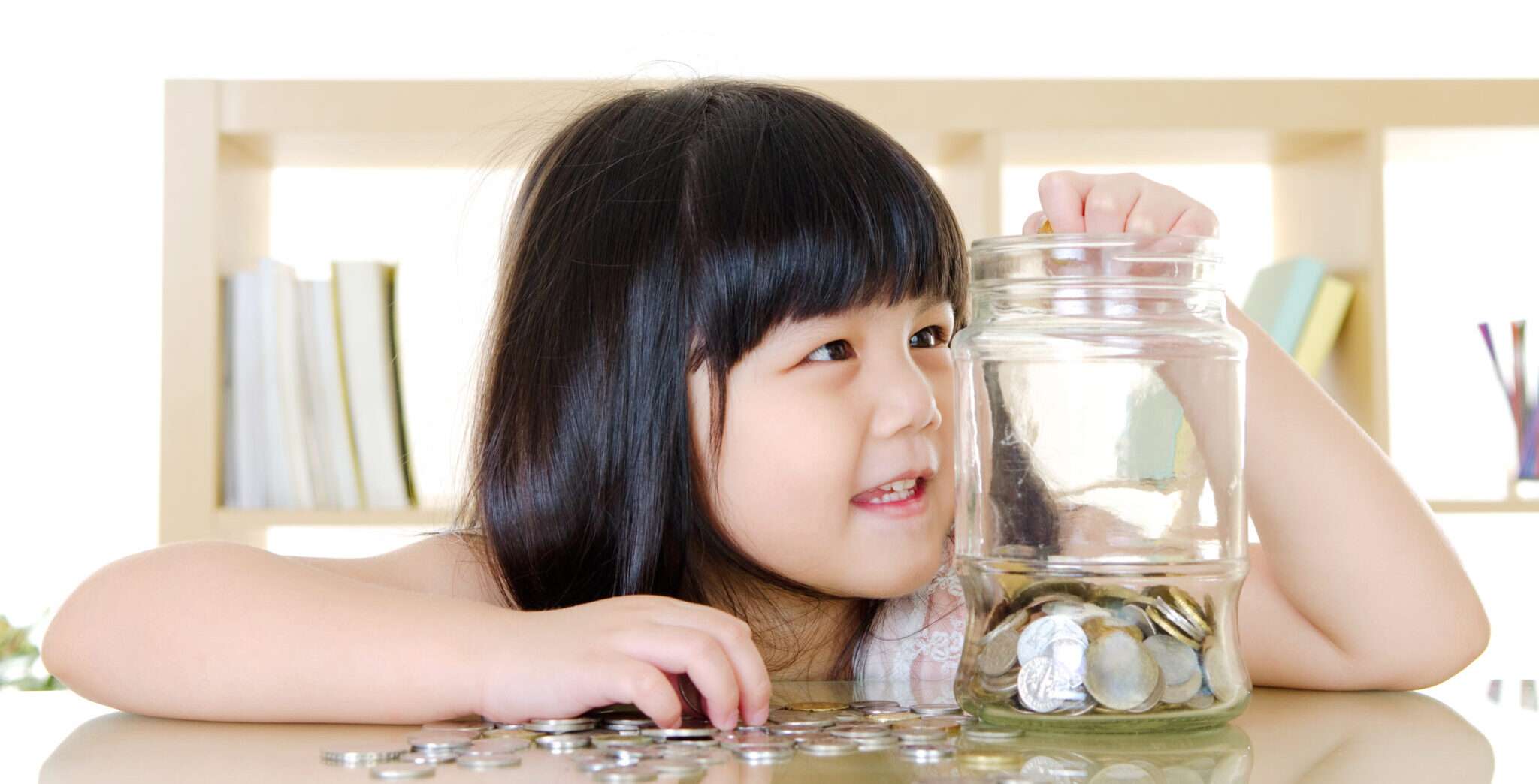 中国から来た小さな女の子がガラスの瓶にコインを慎重に入れています。