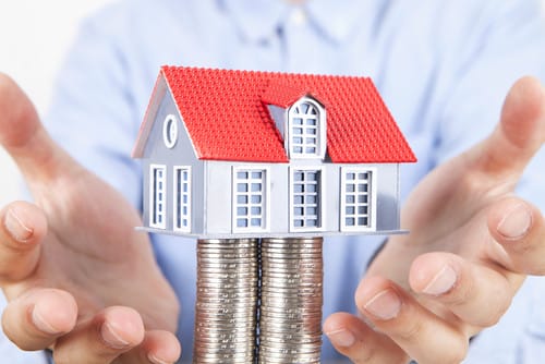 中国のコインの山の上に家の模型を置く男性。