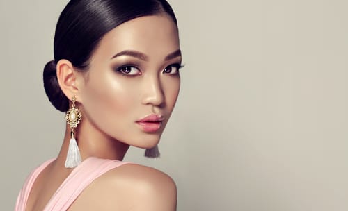 ピンクのドレスを着たアジアの女性がイヤリングでポーズをとる。
