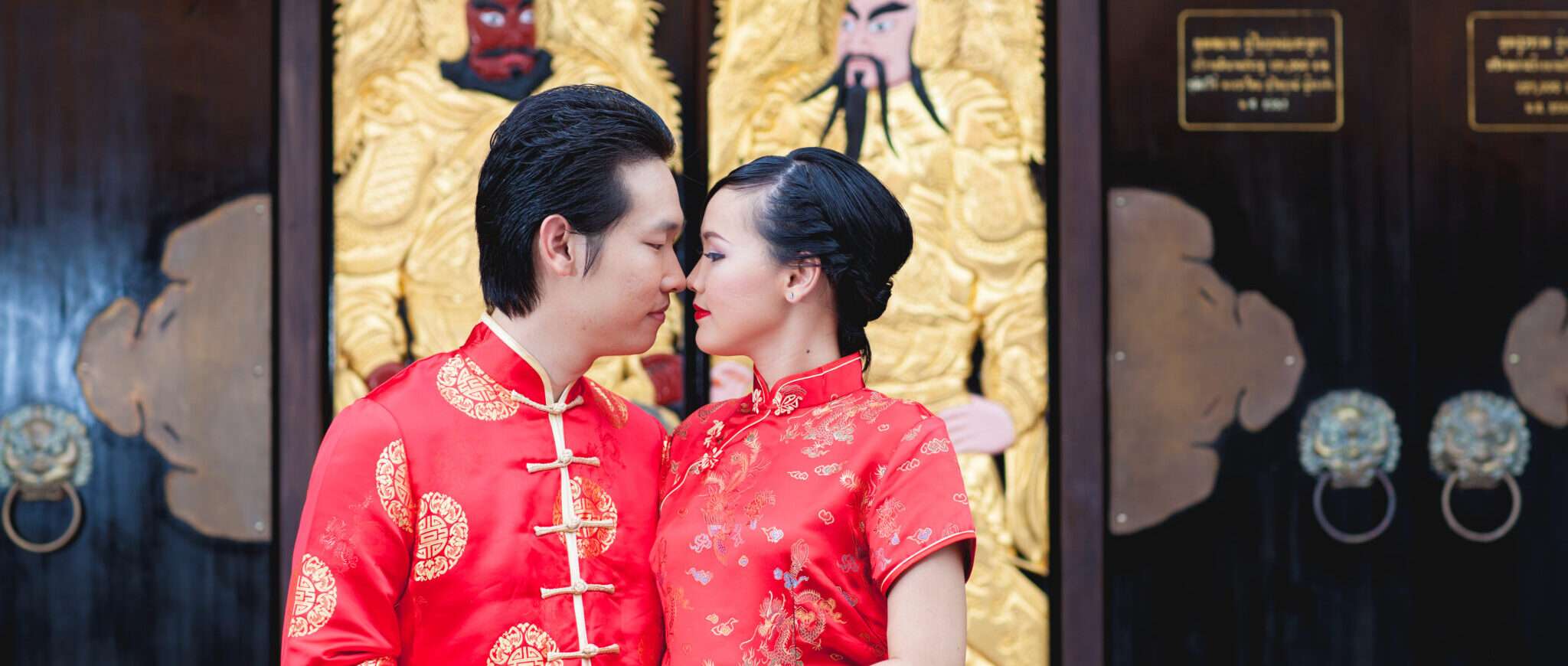中国の服を着たカップルが金色のドアの前でキスをしています。