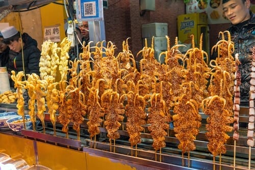 中国では、男性が食べ物の串を持って屋台の前に立っています。