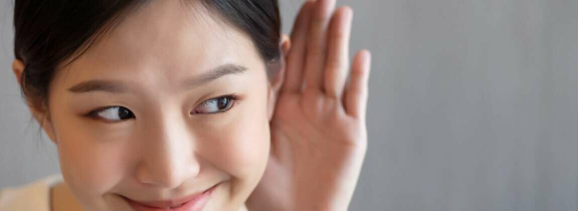 中国出身の若いアジア人女性が耳に手を当てている。