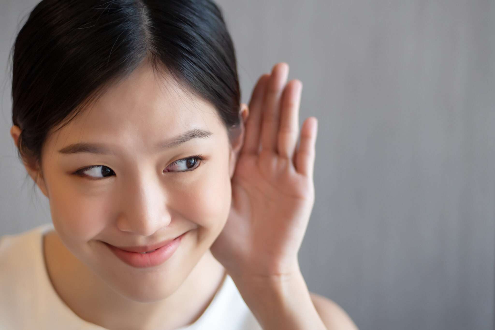 中国出身の若いアジア人女性が耳に手を当てている。