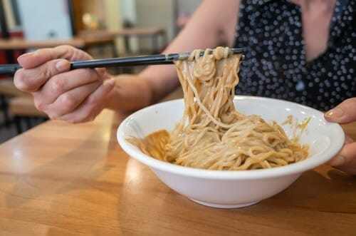 中国で女性が箸で麺の入ったボウルを持っています。