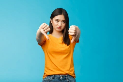 中国(中国)の青い背景にサムダウンサインを表示する若い女性。 中国(中国)の青い背景にサムダウンサインを表示する若い女性。