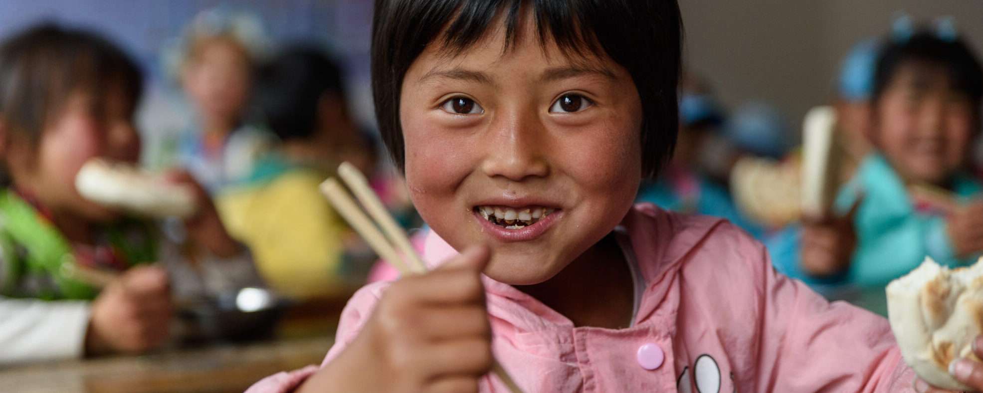 中国の教室の前で、若い女の子が箸を使って食事をしている。