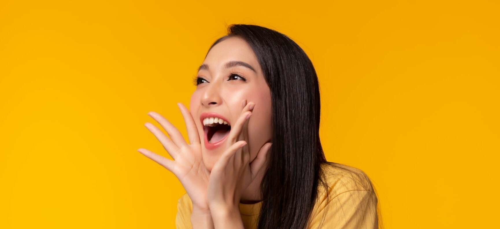 黄色の背景に両手を上げたアジア系の若い女性が、中国の活気に満ちたエネルギーと精神を表しています。