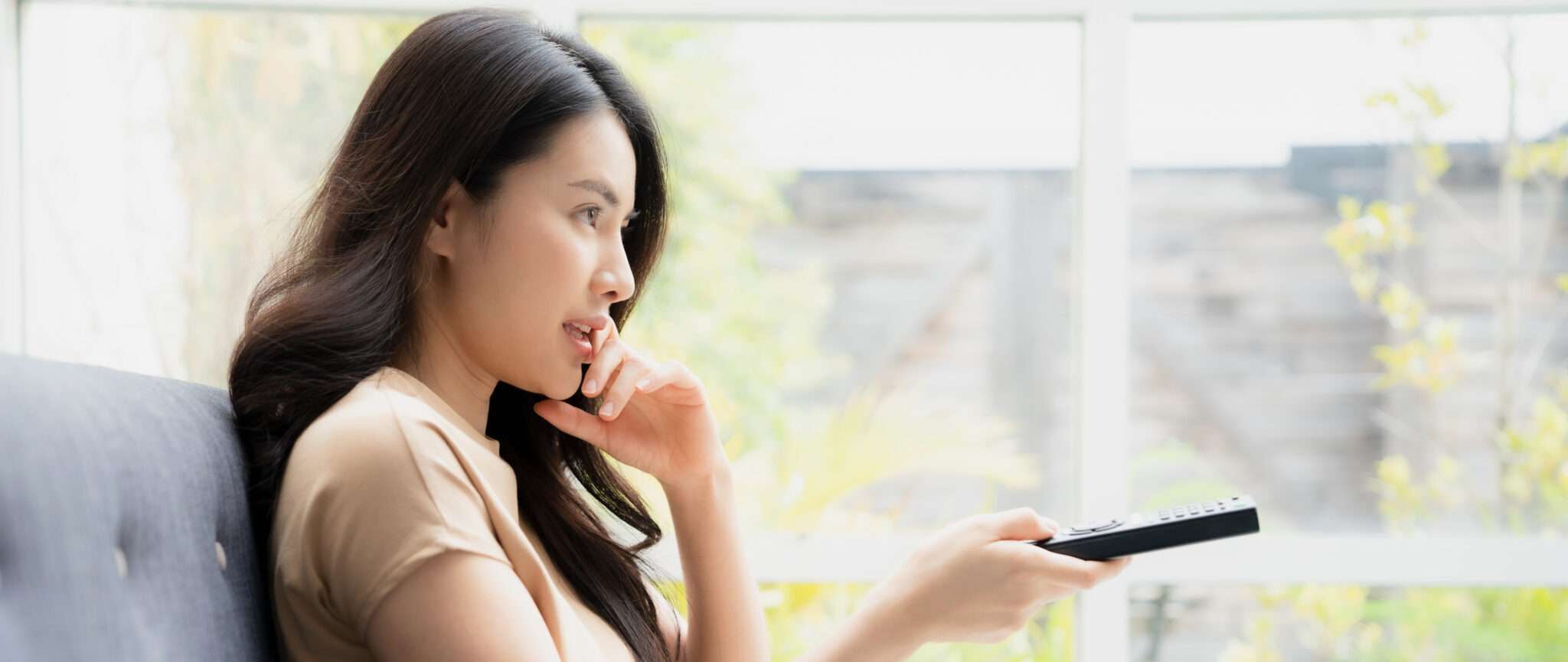 中国の女性がソファに座ってリモコンを持っています。 中国の女性がソファに座ってリモコンを持っています。