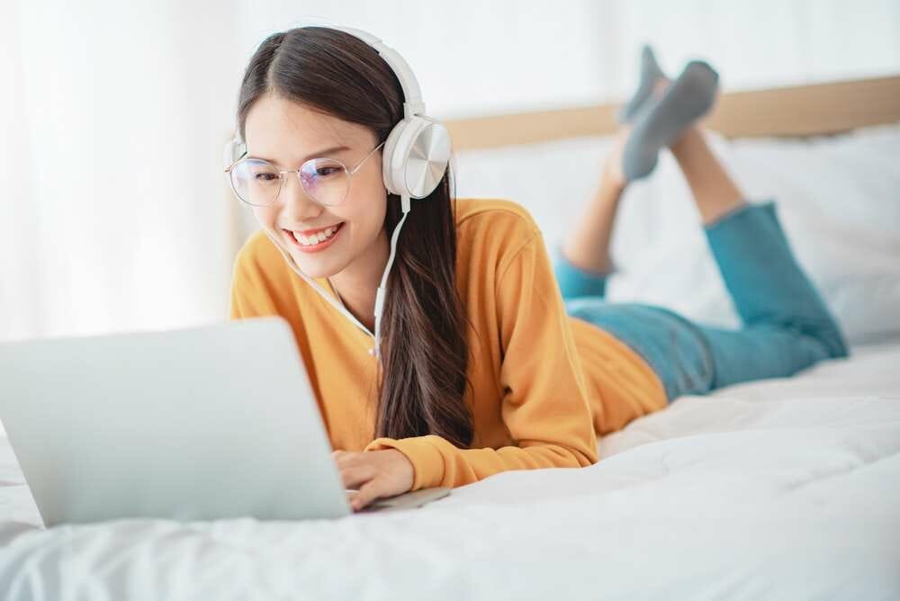 ヘッドフォンとラップトップを持ってベッドに横たわる若い女性。 ヘッドフォンとラップトップを持ってベッドに横たわる若い女性。