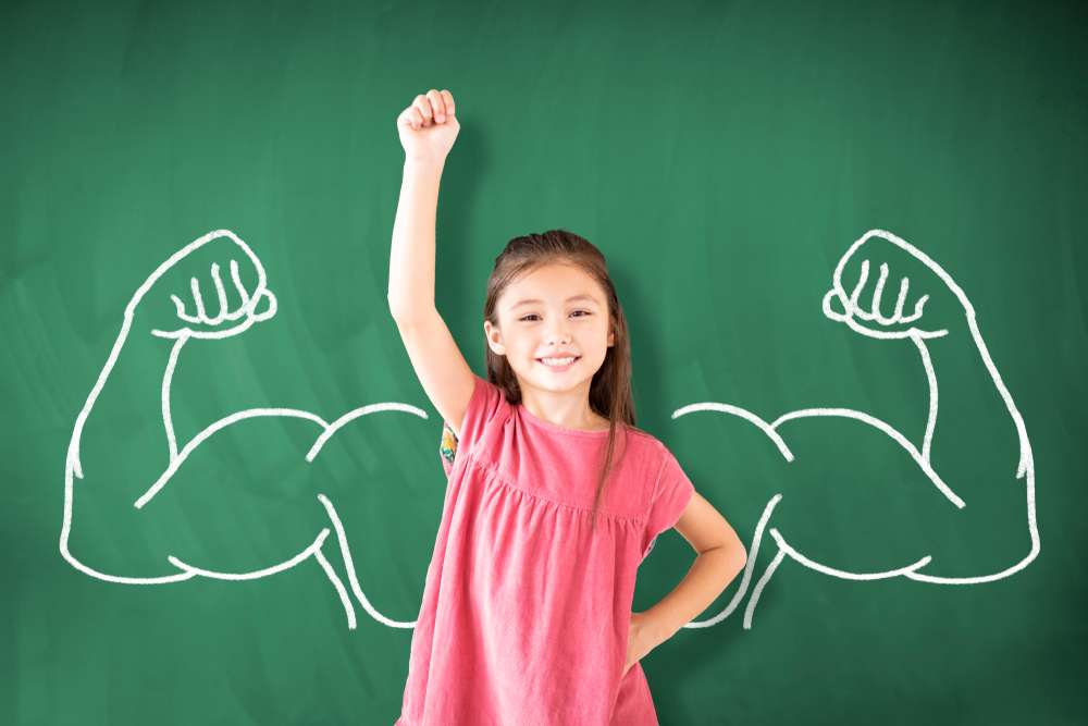 中国から来た小さな女の子が腕の絵を描いた黒板の前に立っています。 中国から来た小さな女の子が腕の絵を描いた黒板の前に立っています。