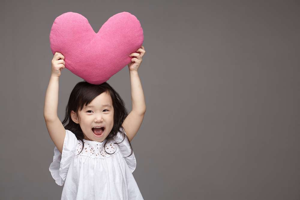 ピンクのハート型の枕を掲げる中国から来た小さな女の子。 ピンクのハート型の枕を掲げる中国から来た小さな女の子。