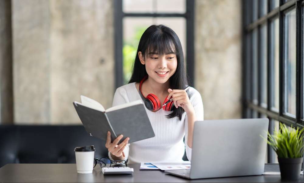 中国の机に座りながら本を読んでいるアジア系の若い女性。 中国の机に座りながら本を読んでいるアジア系の若い女性。