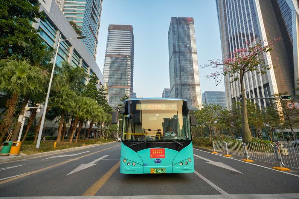 説明：中国城市の街道を走る辣色の公交車で、周囲は高層ビルです。