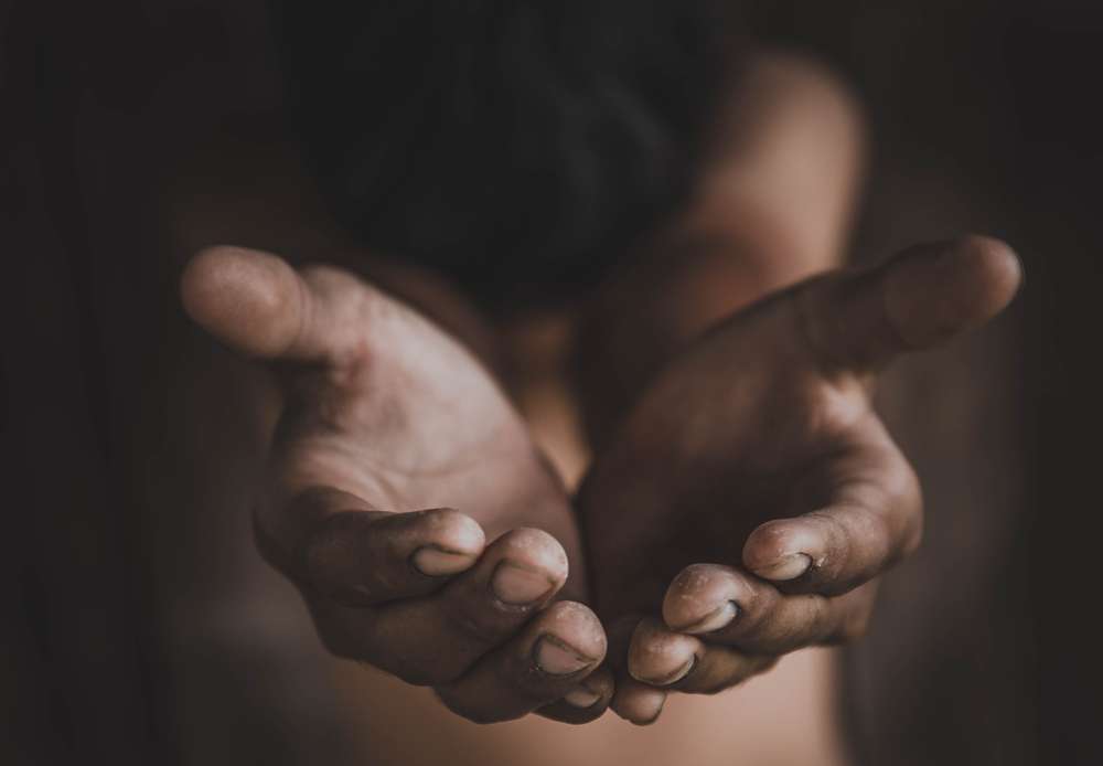 中国で、ぼやけた暗い背景の中で、差し出したり懇願したりしている、伸ばされた汚れた両手のクローズアップ。