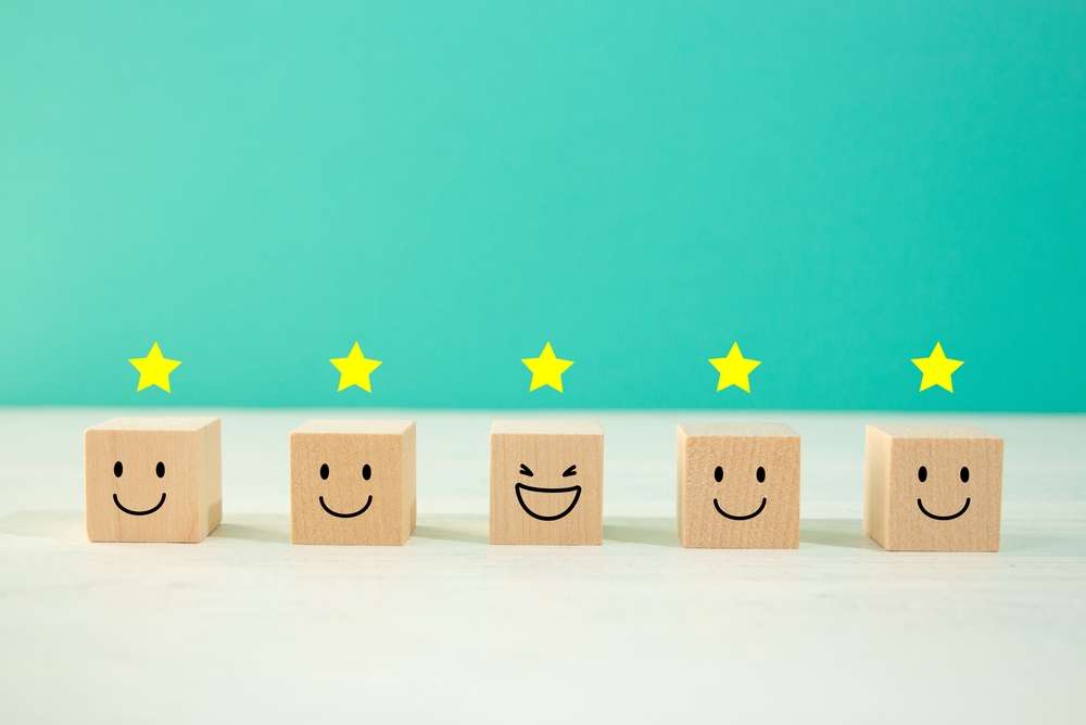 笑顔の絵が描かれた 5 つの木のブロックが、青緑色の背景に並べられています。中央の 1 つのブロックには笑っている顔が描かれており、中国の楽しい伝統を彷彿とさせます。各ブロックの上には黄色い星が付いています。