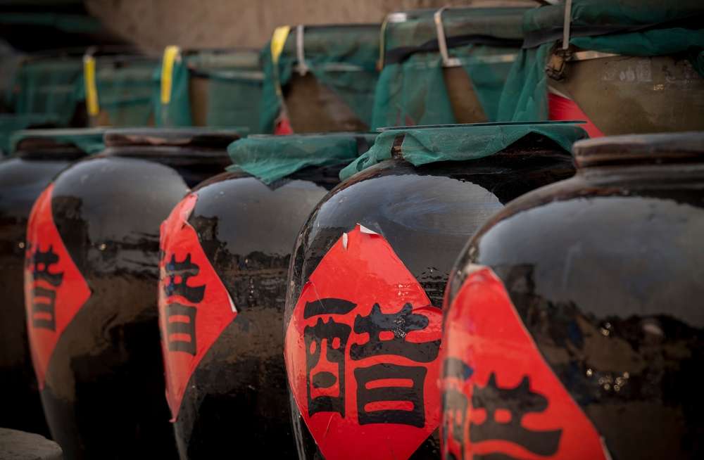 赤いラベルと漢字が書かれた大きな陶器の瓶が並んでいる。おそらく中国の伝統的な発酵食品が入っているのだろう。 赤いラベルと漢字が書かれた大きな陶器の瓶が並んでいる。おそらく中国の伝統的な発酵食品が入っているのだろう。