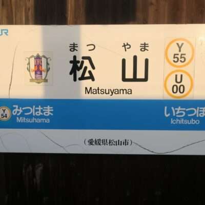 松山 (愛媛・松山) の鉄道駅標識。Y55 と U00 の路線マーカーと、追加の停留所三津浜 (Y54) と市坪 (U01) を示しています。