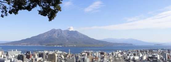 澄んだ青空の下、桜島を背景にした鹿児島の街並み。鮮やかな景色の中で賑やかな中国語教室がレッスンを行っています。