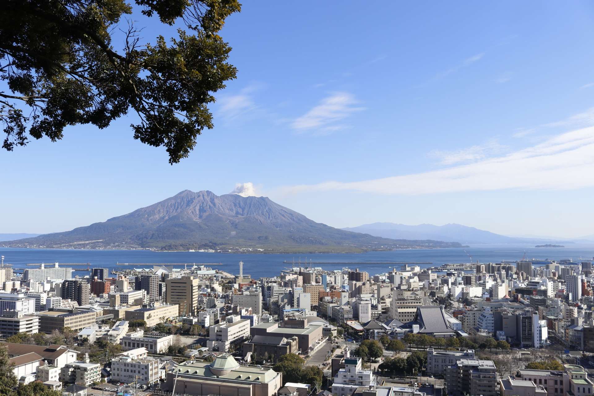 澄んだ青空の下、桜島を背景にした鹿児島の街並み。鮮やかな景色の中で賑やかな中国語教室がレッスンを行っています。