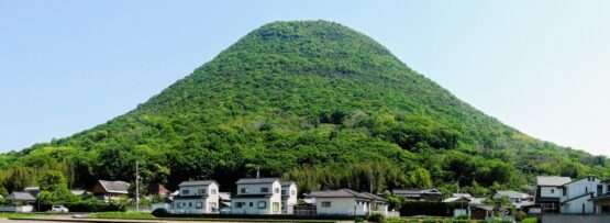 香川・高松の背景には緑豊かな丘がそびえ立ち、手前には澄み切った青空の下、小さな家々と平らな畑が広がっています。近くには活気ある中国語学校があり、この絵のように美しい風景の中で文化交流が活発に行われています。