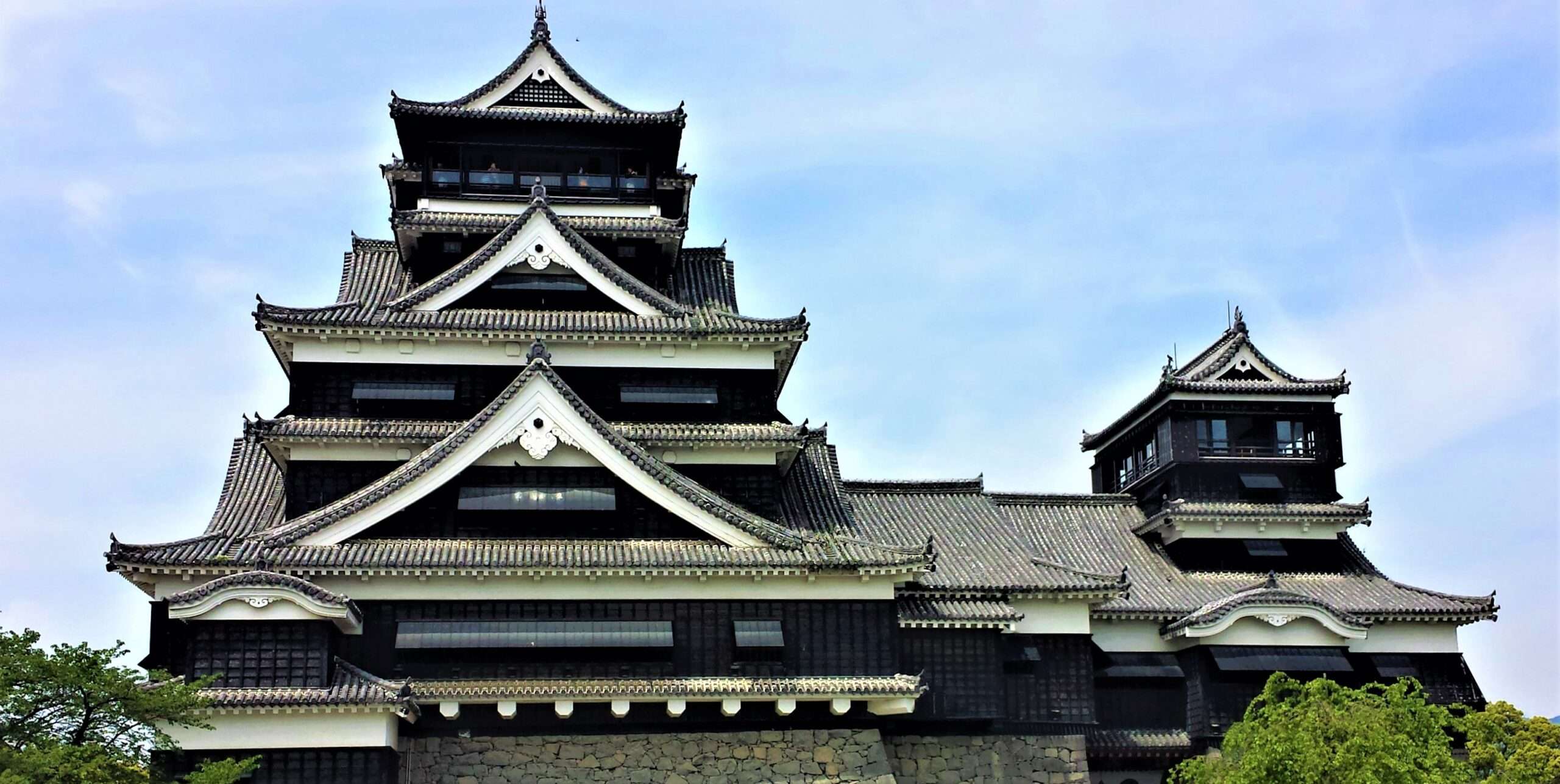 晴れた空を背景に、熊本にある伝統的な日本の城は、華やかな段状の屋根と暗い木製のファサードを誇り、この街の豊かな文化のタペストリーを彷彿とさせます。近くには、歴史的な雰囲気と現代的な学習機会を兼ね備えた活気ある中国語教室があります。