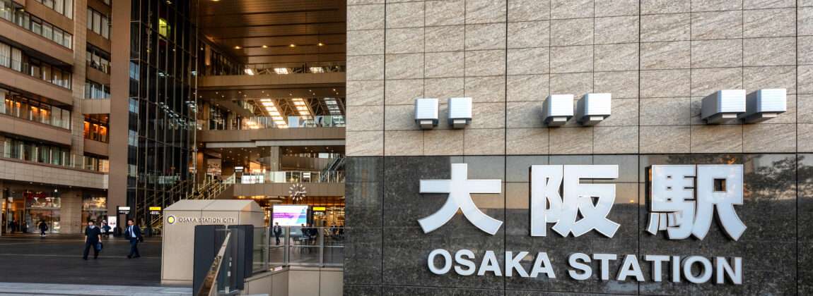 大阪駅の外観とその名前が壁に大きく表示されています。おそらく、賑やかな大阪の近くの中国語教室に向かう人々が入り口付近を歩いています。