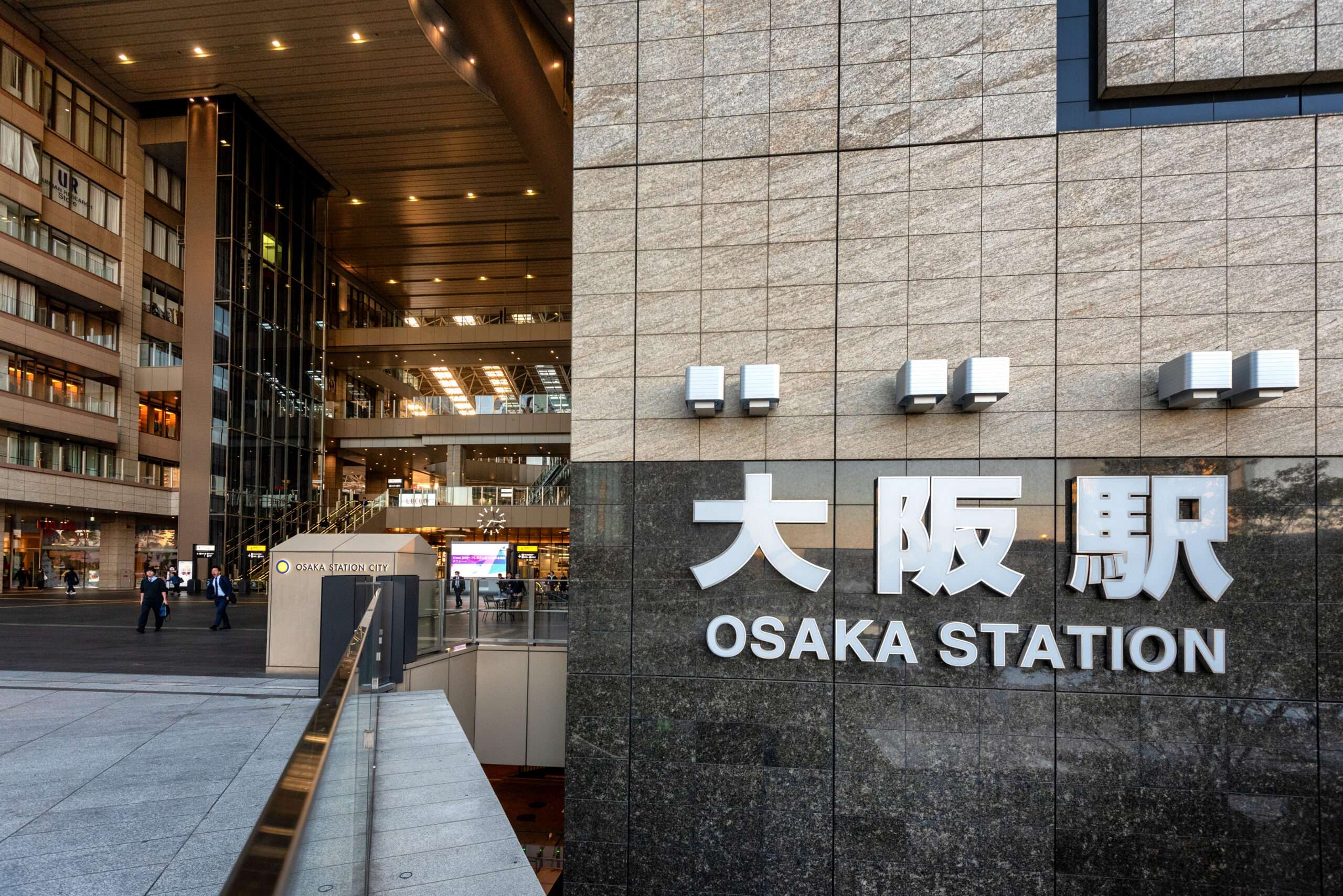 大阪駅の外観とその名前が壁に大きく表示されています。おそらく、賑やかな大阪の近くの中国語教室に向かう人々が入り口付近を歩いています。