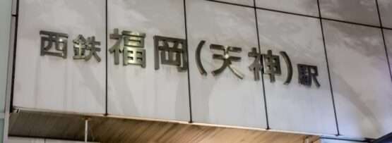 日本の西鉄福岡（天神）駅の入り口にある看板。真っ白なタイル張りの壁に、なめらかな金属の文字が描かれています。近くには、天神の中心で言語と文化が融合する中国語教室があります。