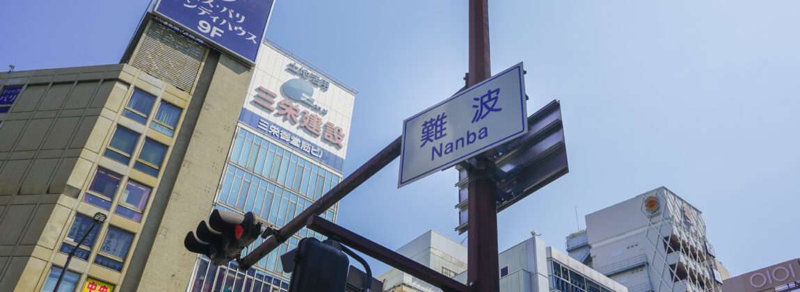 難波のストリート ビュー、難波・なんば。澄んだ青い空の下、信号機と日本の標識で飾られた高層ビルが特徴です。賑やかな通りの中に、中国語を習得するために熱心な学習者が集まる中国語教室があります。 難波のストリート ビュー、難波・なんば。澄んだ青い空の下、信号機と日本の標識で飾られた高層ビルが特徴です。賑やかな通りの中に、中国語を習得するために熱心な学習者が集まる中国語教室があります。