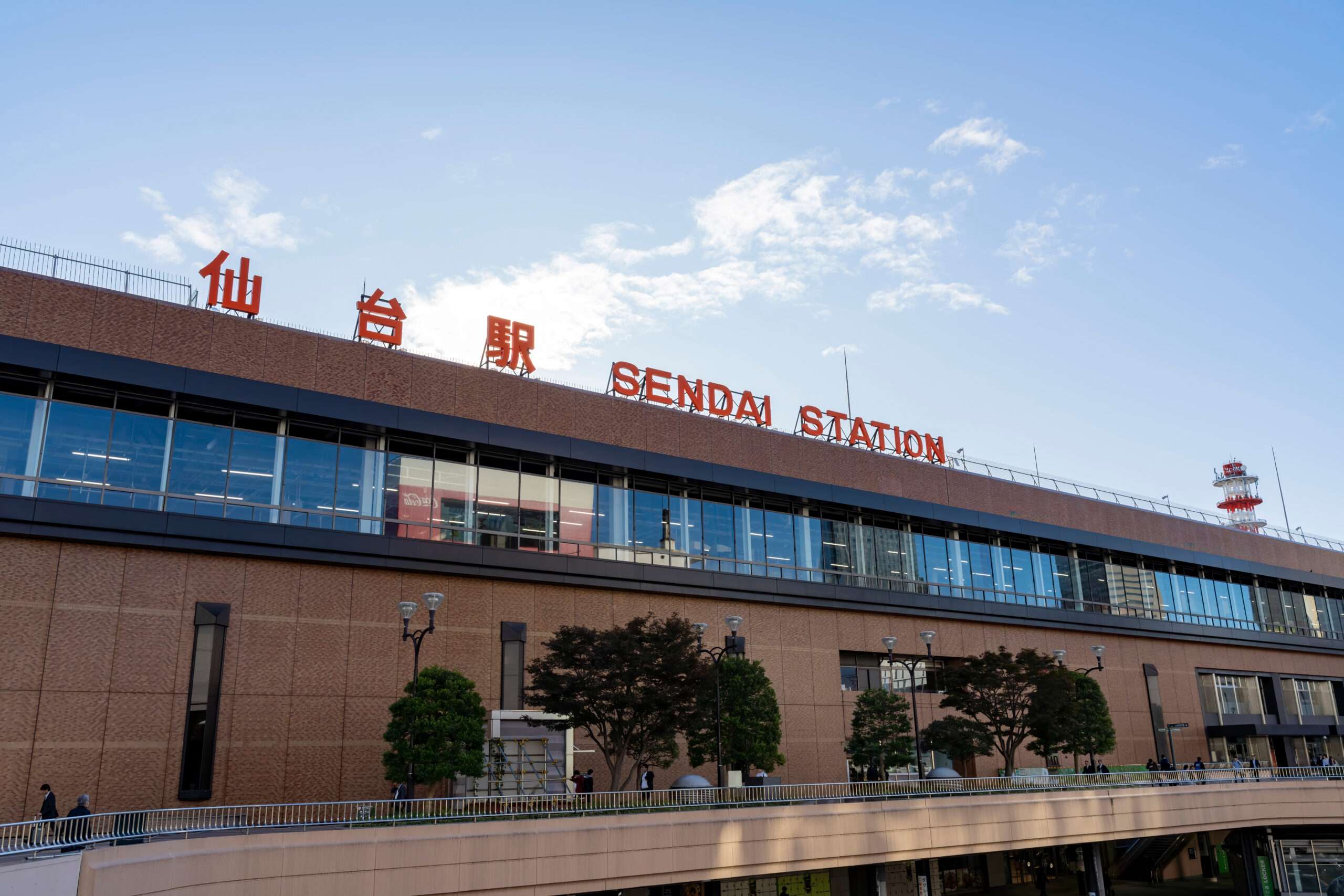 曇り空の下、大きな赤い看板が目印の、宮城・仙台の重要なランドマークである仙台駅の外観。