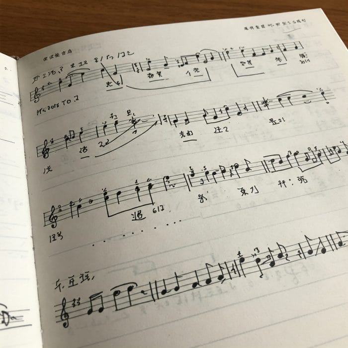 楽譜と中国語の歌詞が書かれたノートがあり、音符と声調記号が比較されている