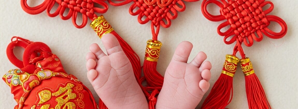 明るい背景に、赤い中国結びとタッセルに囲まれた赤ちゃんの足。.