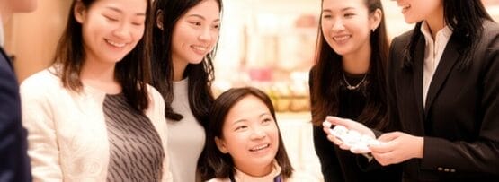 5人の女性のグループが、明るい室内で小さな置物を展示したテーブルの周りに立ち、微笑みながら会話を交わしています。.