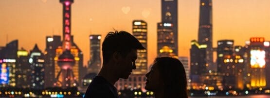 夕暮れ時に、街のスカイラインとハート型の光を背景に、カップルが向かい合って立っています。.