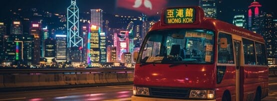 旺角」と書かれた赤いミニバスが濡れた夜道を走り、背景には香港のスカイラインと大きな香港国旗がライトアップされている。.