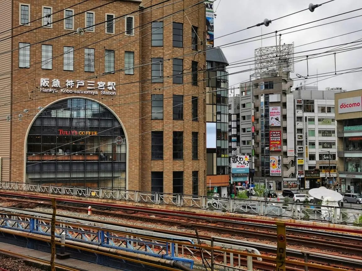 阪急神戸三宮駅と茶色のレンガ造りのタリーズコーヒーを望む。手前に線路、奥に街のビル。.