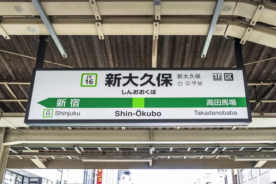新大久保の駅ホームには、新宿と高田馬場への案内が日本語、英語、韓国語で表示されている。.